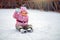 Girl shod in figure skates, sits on ice on a skating rink and waves a hand