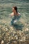 A girl in a shoulder-length denim jumpsuit stands in seawater. Her gaze is directed to the side