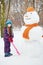 Girl with shovel stands next to big snowman