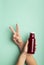 Girl showing v sign and advertising Glass bottle with beet smoothie