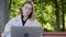 Girl sits on a bench in autumn, writing on a laptop and looking around smiling