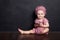 The girl sits on a brown floor and holds phone. The girl looks in the camera and smilles. Black background