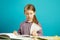 Girl sits on desk in the classroom, turns page of textbook, holds pencil, over blue background. Schoolchild in