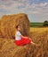 A girl sits in a field next to a haystack.