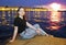 The girl sits on the granite steps against the background of the evening city on the embankment of the Neva river. Saint-