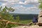 The girl sits on a horizontally growing pine tree on the edge of a cliff