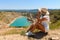 A girl sits and looks in the mountains at a blue lake in the shape of a heart.