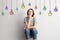 Girl sits near wall on background of colored drawn bulbs