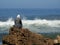 A girl sits on the rock watching the waves