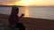 Girl sits on the shore of the sea and drinks a hot tea. Amazing golden sunset