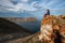 A girl sits on the stones of a high rock near Lake Baikal against the sky with beautiful clouds.