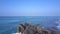 Girl sits in yoga pose on large rocky cliff washed by ocean