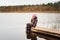 Girl sitting alone at wooden footbridge of a forest lake