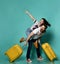 Girl sitting on back of her boyfriend and pointing somwhere, they are screaming, guy holding two yellow suitcases. Blue background