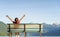 Girl sitting on a bench with her arms up with stalk hat on and red dress relaxing looking at the mountains by a lake