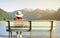 Girl sitting on a bench with stalk hat on and red dress relaxing looking at the mountains by a lake