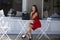 Girl sitting on the chair in chic shoes with a stylish black bag and red dress