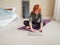 Girl sitting cross-legged on the floor at home in bedroom. Woman on yoga mat opening laptop. Active lifestyle concept in