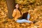 Girl sitting on fall leaves in city park and working on laptop. Concept of autumn warmth, atmosphere and comfort, working in