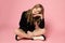 Girl sitting on floor with legs crossed. Full length studio shot on pink background. Looking into frame