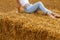 Girl sitting on a haystack on a bale in the agricultural field after harvesting