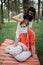 Girl sitting on mat in park while woman is placing medical mask