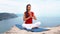 Girl sitting on rock by sea, meditating in lotus yoga pose, concentrating, relaxing mind, soul and body.