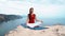 Girl sitting on rock by sea, meditating in lotus yoga pose, concentrating, relaxing mind, soul and body.