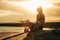 girl sitting on rock with surfboard on beach at sunset with airplane