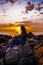 girl sitting on the rocks on the shore and watching colorful sunset in the ocean. side view portrait of young woman in casual