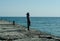 The girl is sitting on the seashore. Girl resting by the sea. A woman is standing on the pier.