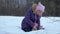 Girl sitting on snow in winter forest and making snowman