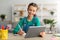 Girl sitting at table, using tablet, writing in notebook