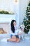 Girl sitting with white labrador near decorated fireplace and Christmas tree.