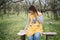 Girl sitting on wooden bench in front of orchard