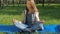 A girl is sitting in a yoga pose in the park. A teenage girl with freckles meditates. A young girl in jeans outdoors on the carpet