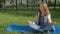 A girl is sitting in a yoga pose in the park. A teenage girl with freckles meditates. A young girl in jeans outdoors on the carpet