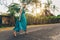 A girl of size in a long blue dress runs barefoot on the track against a backdrop of palm trees and villas