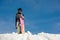 Girl in ski goggles and ski equipment stands in the snow against the blue sky