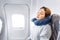 Girl sleeping in her seat on the plane near the window in a mask and with a pillow to sleep. The concept of travel with