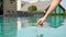 The girl slowly lowers her index finger into the pool water and quickly takes it out. checks the temperature of the pool water