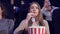 Girl slowly puts the popcorn in her mouth at the movie theater