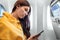 A girl with a smartphone in front of an airplane window, the cabin of a passenger airliner. Using gadgets in flight, airplane mode