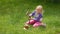 Girl smashes coconut with a heavy iron hammer sitting on the grass.