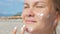 Girl smears her face skin with sunblock cream while standing on a sandy beach.