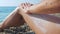 Girl smears her leg with sunblock cream while lying on a pebble beach.