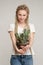 Girl smiles and holds  cactus in her hands, potted green plant, hair girl braided in dreadlocks