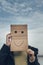 Girl with a smiling cardboard face on the background of clouds