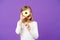 Girl on smiling face holds sweet donut in hand, violet background. Kid girl with long hair likes sweets and treats