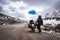 Girl solo ridder in ridding gears with loaded motorcycle at isolated road and snow cap mountains